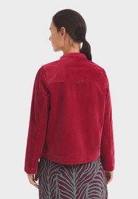 Rode corduroy jas met een knoopkraag, lange mouwen en een rechte snit. Opmerkelijke verticale ribbels in de stof.