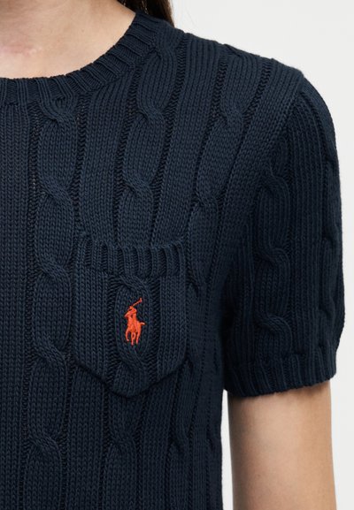 Laivastonsininen neulepusero, jossa on punoskuvio, lyhyet hihat, resorinen pyöreä pääntie ja pieni oranssi Polo-logo rintataskussa.