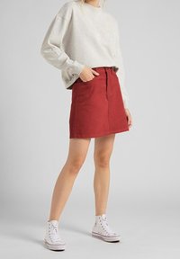 Mini falda de pana roja con bolsillos frontales, combinada con un sudadera oversized gris claro y zapatillas altas blancas.