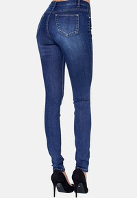 Jeans skinny de color azul oscuro con una textura de denim suave, que cuentan con dos bolsillos traseros y un diseño de cintura alta, combinados con tacones de aguja negros.