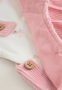 Vaaleanpunainen puuvillasekoitekangas, jossa on pehmeä pinta, röyhelökoristeet, puunapit ja kukkakuosi valkoisella kankaalla.