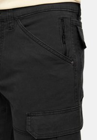 Shorts cargo noirs en tissu robuste, dotés d'une poche zippée, de poches latérales et de coutures décoratives.