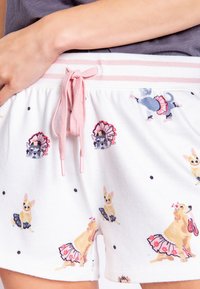 White shorts featuring colorful dog prints in various poses, with a pink drawstring and striped waistband. Soft, lightweight fabric.