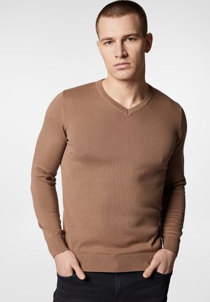 Brązowy sweter z dekoltem w serek, z długimi rękawami, ribbowymi mankietami i dołem, dopasowany fason, wykonany z teksturowanej dzianiny, noszony z czarmi spodniami.