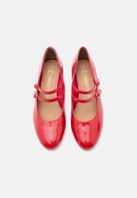 Ζευγάρι λαμπερών κόκκινων παπουτσιών Mary Jane με διπλές λουράκια και πόρπες, μέγεθος 37, φαίνoνται από πάνω σε λευκό φόντο.