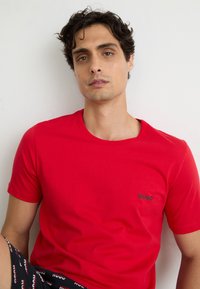 Rotes Baumwoll-T-Shirt mit rundem Halsausschnitt und kurzen Ärmeln, mit einem kleinen schwarzen "HUGO"-Logo auf der linken Brustseite.