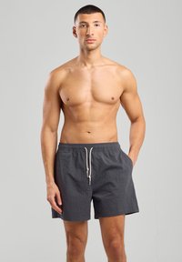 Harmaat uintihousut, joissa on teksturoitu kangas, joustava vyötärö ja nauhakiinnitys. Sisältää sivutaskut ja rennon mitoituksen.