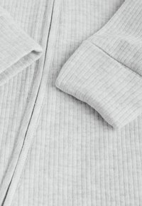 Tessuto per abbigliamento grigio a costine con una cucitura centrale visibile e dettagli ai polsini. Texture morbida, leggero, con righe verticali.