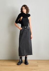 Bodysuit negro combinado con una falda larga de mezclilla gris oscuro de talle alto con dobladillo deshilachado, y llevada con botas negras hasta el tobillo.