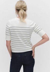 Hvid strikket sweater med vandrette marineblå striber, korte ærmer og ribbet kant, parret med mørk denim jeans, vist fra ryggen.