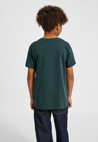 Mørkegrøn bomulds-T-shirt med korte ærmer og rund halsudskæring, kombineret med mørkeblå jeans. Stoffet virker glat med en afslappet pasform.