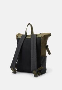 Sac à dos fabriqué en maille noire et matériel synthétique vert olive. Il dispose de sangles réglables et d'un design à rabat. Forme arrondie et structurée.