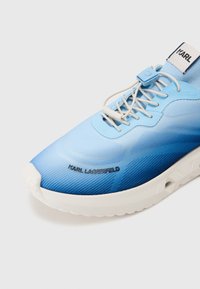 Blue sneaker with gradient texture, featuring a smooth upper, white sole, and "KARL LAGERFELD" logo. Lacing and plastic accents visible.
