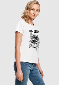 Hvid bomulds t-shirt med en sort grafik af en rose og teksten "THIN LIZZY" i stiliseret skrift. Korte ærmer og afslappet pasform.
