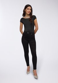 Body a maniche corte nera con texture a pois, abbinato a jeans neri aderenti e scarpe con tacco beige glitterate. Collana argento in evidenza.