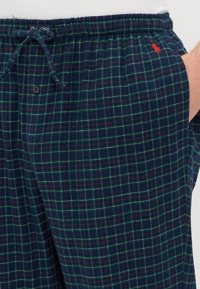 Calças de pijama em padrão xadrez azul marinho com uma grelha verde e vermelha, cintura elástica com cordão de ajuste e pequeno detalhe do logótipos vermelho.