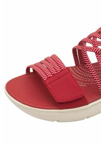 Sandal rossa con cinturini in tessuto intrecciato, suola rossa liscia e una fascia con chiusura a velcro per una vestibilità sicura. Suola bianca spessa e curva.
