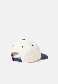 Fehér baseball sapka kék nappal és gombbal, csattal záródik és szellőző lyukakkal rendelkezik. Textúrált anyaggal, sima peremmel.