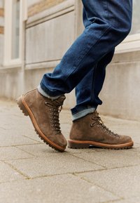 Brązowe zamszowe buty trekkingowe z metalowymi oczkami, dopasowanymi sznurowadłami i ciężką gumową podeszwą, zestawione z podwiniętymi dżinsami.