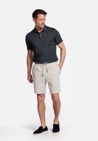 Donkergrijze polo met een borstzak, gecombineerd met lichtbeige shorts met een trekkoord en zwarte instapschoenen. Eenvoudig en casual ontwerp.