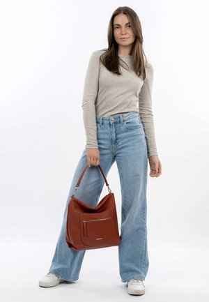 Brown leather shoulder bag with a textured finish, featuring a zippered pocket and a wide strap, held by a model wearing light denim.