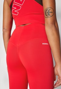 Completo sportivo rosso composto da un top corto aderente e leggins a vita alta. Il materiale è liscio con una finitura opaca, con un logo visibile sulla cintura.