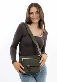 Zelená látková crossbody taška s přední kapsou na zip, hnědými koženými akcenty, nastavitelným popruhem a obdélníkovým tvarem.