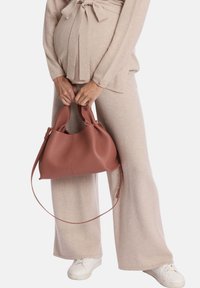 Ensemble en crème, composé d'un pull doux et d'un pantalon ; tenant un sac en cuir texturé rose avec deux poignées et une bandoulière amovible.