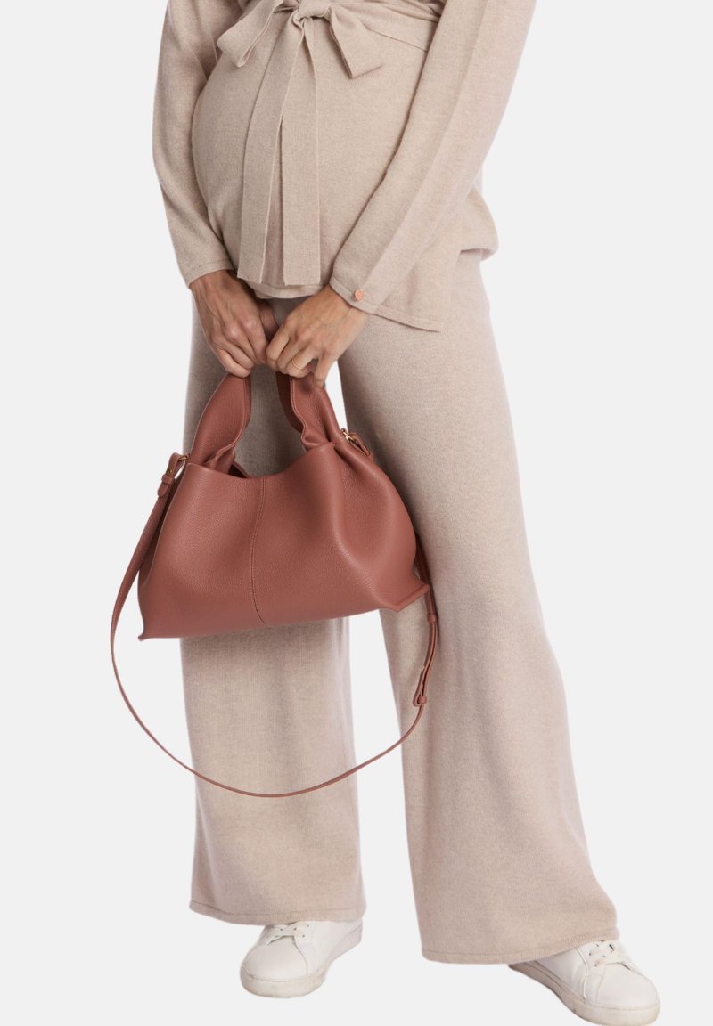 Cremefarbenes, weiches Sweater- und Hosen-Set; hält eine strukturierte, rosefarbene Ledertasche mit zwei Griffen und einem abnehmbaren Schultergurt.