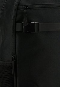 Czarny plecak z tkaniny z zamykaną kieszenią, regulowanym paskiem z klamrą, siatkową kieszenią boczną oraz gładkim materiałem.