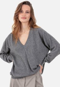 Pull gris en tricot avec col en V, coupe ample et texture subtile. Le design présente des épaules tombantes et des poignets côtelés.