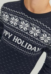 Námorně modrý pletený svetr s bílými vzory sněhových vloček a textem "ŠŤASTNÉ VÁNOCE" v tučném písmu. Hladký nákrčník a texturovaný design.