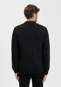 Zwarte gebreide trui met een ronde hals, voorzien van een gestructureerd patroon en versleten accenten op de mouwen, geribbelde zoom en manchetten.