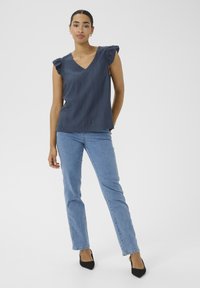 Top sans manches bleu marine avec un décolleté en V et des manches volantes, associé à un jean bleu clair à jambe droite et des escarpins noirs à talons pointus.