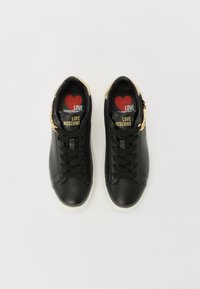 Black leather sneakers with a smooth texture, white rubber soles, gold hardware accents, and red insoles featuring a heart design.