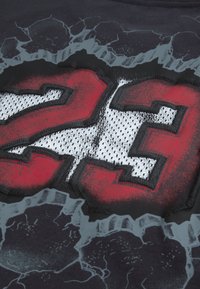 Μαύρο μπλουζάκι με μεγάλο κείμενο "23" σε κόκκινο και λευκό, μ ε ανάγλυφη υφή· το σχέδιο περιλαμβάνει ραγισμένο μοτίβο στο φόντο.