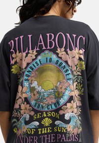 Μαύρο μπλουζάκι με πολύχρωμα λουλουδένια γραφικά και κείμενο. Το σχέδιο περιλαμβάνει ήλιο, κύματα και στρογγυλή σφραγίδα με την ένδειξη "BILLABONG" σε εμφανές σημείο.