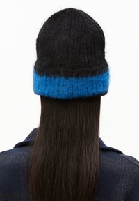 Gebreide muts met een hoge, zwarte kroon en een pluche, blauwe geribbelde band. De textuur is zacht en het kleurcontrast is opvallend.