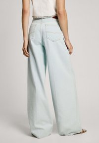 Vaaleansiniset leveälahkeiset farkut, joissa on korkea vyötärö, kaksi takataskua ja siisti viimeistely. Yhdistetty kropattuun toppiin ja neutraaleihin sandaaleihin.