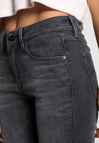 Šedé džíny z denimu s úzkým střihem, výrazným prošitím, předními kapsami a zapínáním na knoflíky. Tkanina vypadá měkce s mírně vybledlým vzhledem.