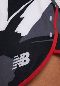 Close-up of black, white, and gray athletic fabric with New Balance logo and red trim on a piece of clothing.