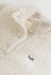 Cremefarbener Fleece-Pullover mit weichem, strukturiertem Finish. Verfügt über einen Kragen, zwei Knöpfe und ein gesticktes "Self."-Logo in Dunkelblau.