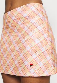 Falda de cuadros en tonos naranja y rosa, hecha de tejido ligero. Presenta un dobladillo con un pequeño logotipo bordado en la parte inferior izquierda.