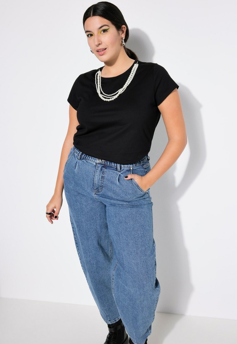 Zwarte katoenen t-shirt gecombineerd met blauwe wijde denim jeans. Een gelaagde witte kralenketting en zwarte enkellaarsjes maken de look compleet.