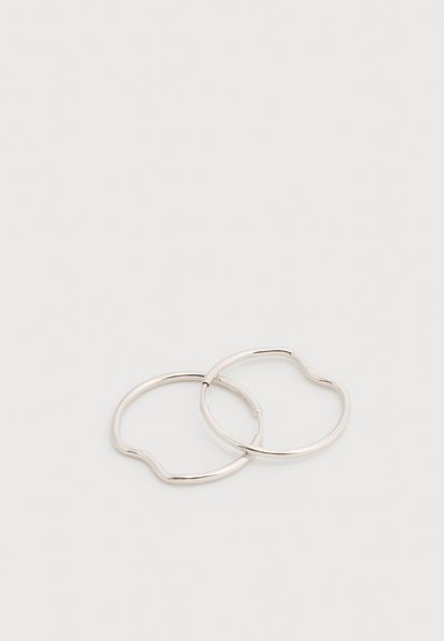 Δύο λεπτοί ασημένιοι μεταλλικοί κρίκοι σκουλαρικιών με μικρές καμπυλωτές εσοχές, τοποθετημένοι αλληλοεπικαλυπτόμενοι σε ένα απλό λευκό φόντο.