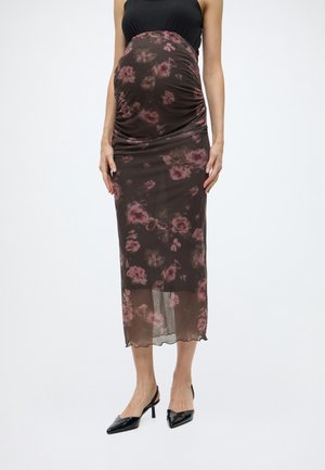 Gravid kvinde iført en blomsteret brun midi nederdel med lagdelt design og sort ærmeløs top, kombineret med sorte spidse hæle.