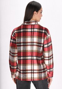 Rood en witte geruite flanellen overhemd met bruine en zwarte accenten. Voorzien van een kraag, lange mouwen en een relaxed pasvorm. Zachte textuur.