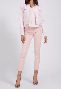 Chaqueta de mezclilla rosa claro con bolsillos delanteros, combinada con una blusa peplum rosa claro y pantalones ajustados rosas. Destacan unos tacones altos de estampado de serpiente.
