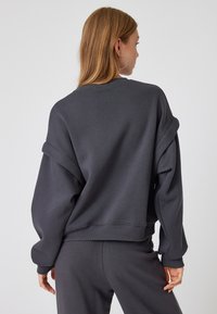 Sudadera oversize de color gris oscuro con puños doblados, dobladillo acanalado y textura de tela suave. Diseño elegante y casual, adecuado para llevar en capas.