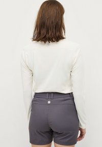 Witte lange mouwen top gecombineerd met grijze shorts. De shorts hebben een tailleband en een decoratieve accent aan de achterkant. Over het algemeen een gladde textuur.